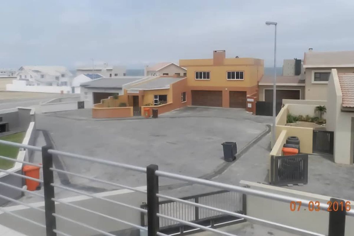 Elevated view overlooking a residential street and neighbouring properties, featuring paved driveways, garage doors, and boundary walls.