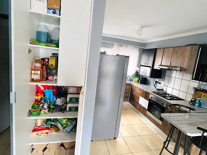 A functional kitchen featuring tiled flooring, built-in cabinetry, a gas hob with extractor fan, and a dedicated pantry cupboard for storage.
