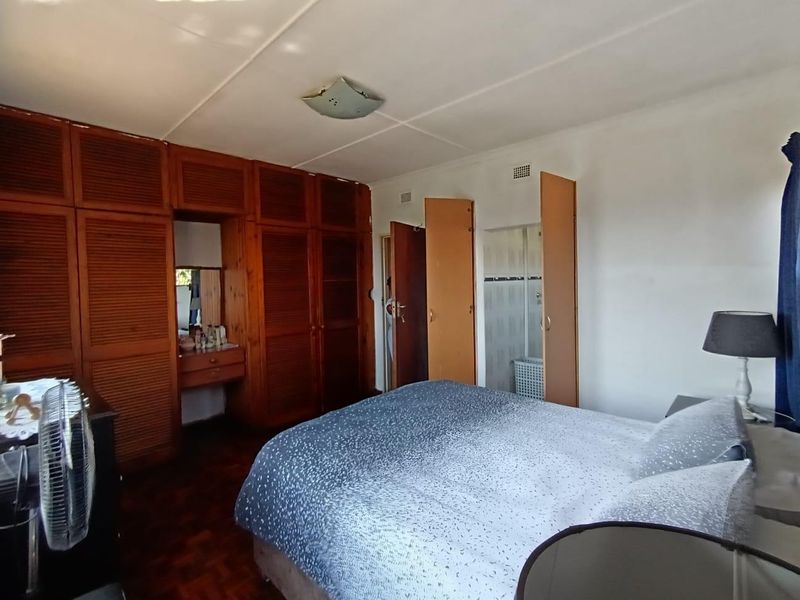 Spacious bedroom featuring extensive built-in wooden cabinetry, parquet flooring, and direct access to an en-suite bathroom.