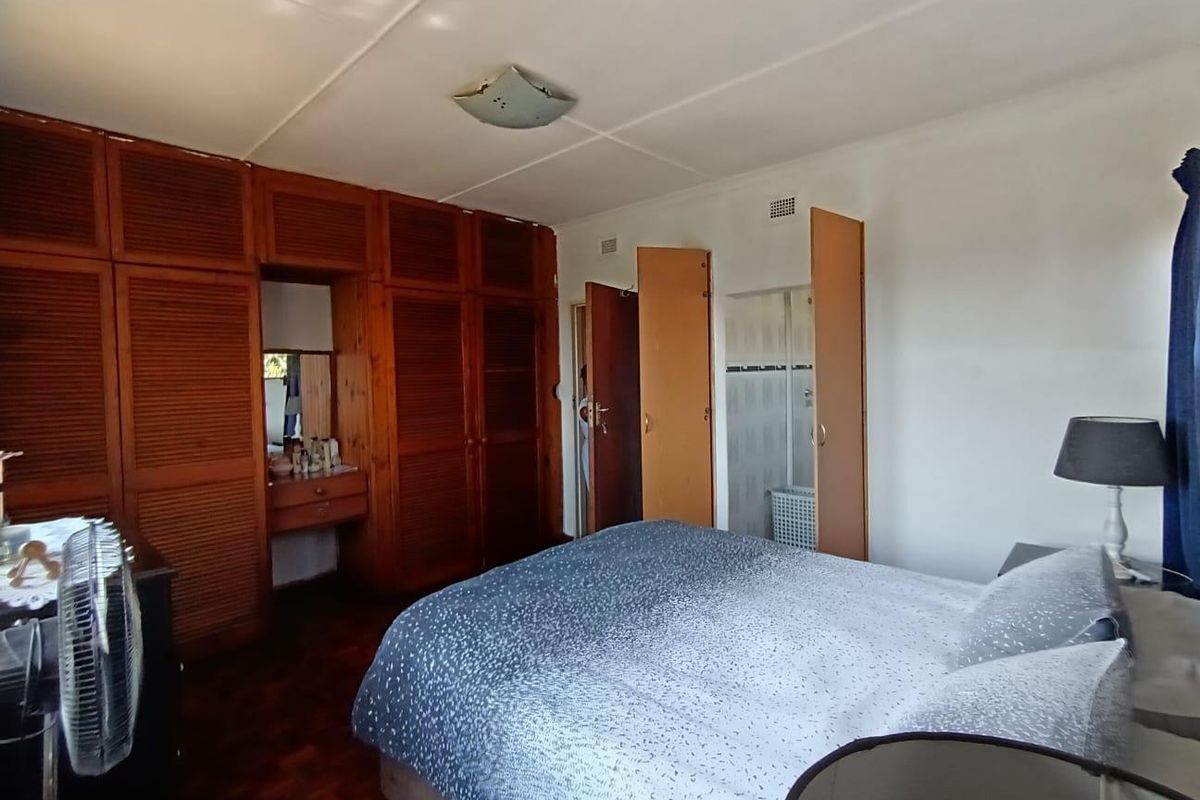 Spacious bedroom featuring extensive built-in wooden cabinetry, parquet flooring, and direct access to an en-suite bathroom.