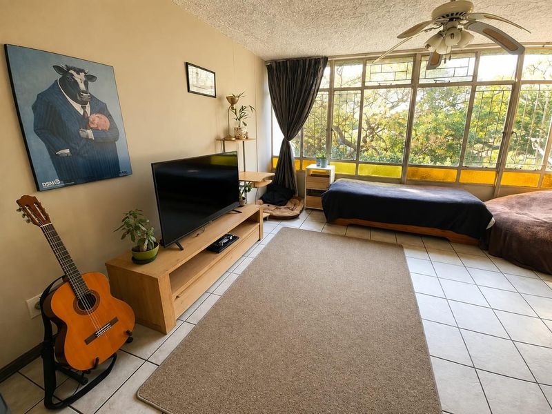A living room featuring large metal-framed windows that provide ample natural light, tiled flooring, and a ceiling fan.