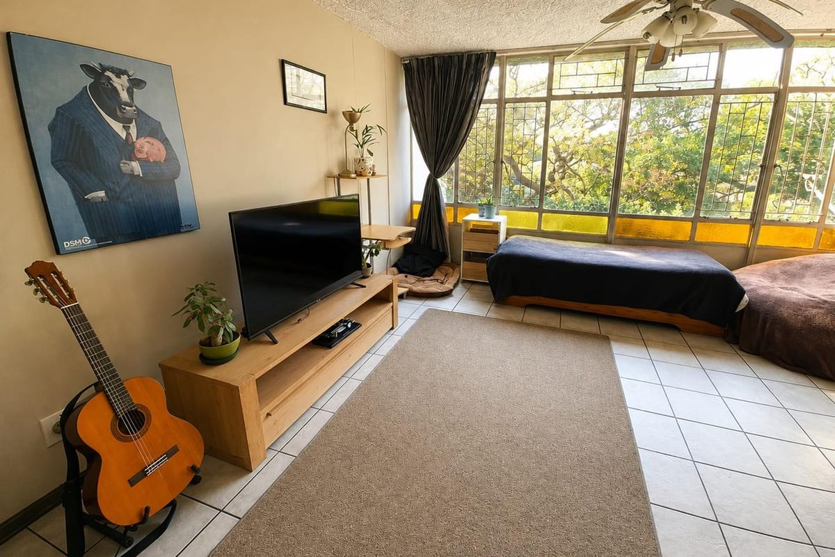 A living room featuring large metal-framed windows that provide ample natural light, tiled flooring, and a ceiling fan.