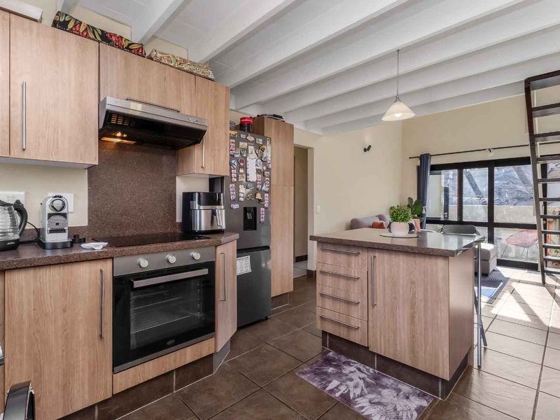 Open-plan kitchen featuring wood-finish cabinetry, built-in appliances, and a central island, flowing into a living area with exposed ceiling beams and natural light.