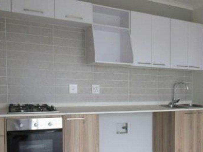 Modern kitchen featuring light wood-tone cabinetry, white upper cabinets, a gas hob, built-in oven, and a neutral tiled backsplash.