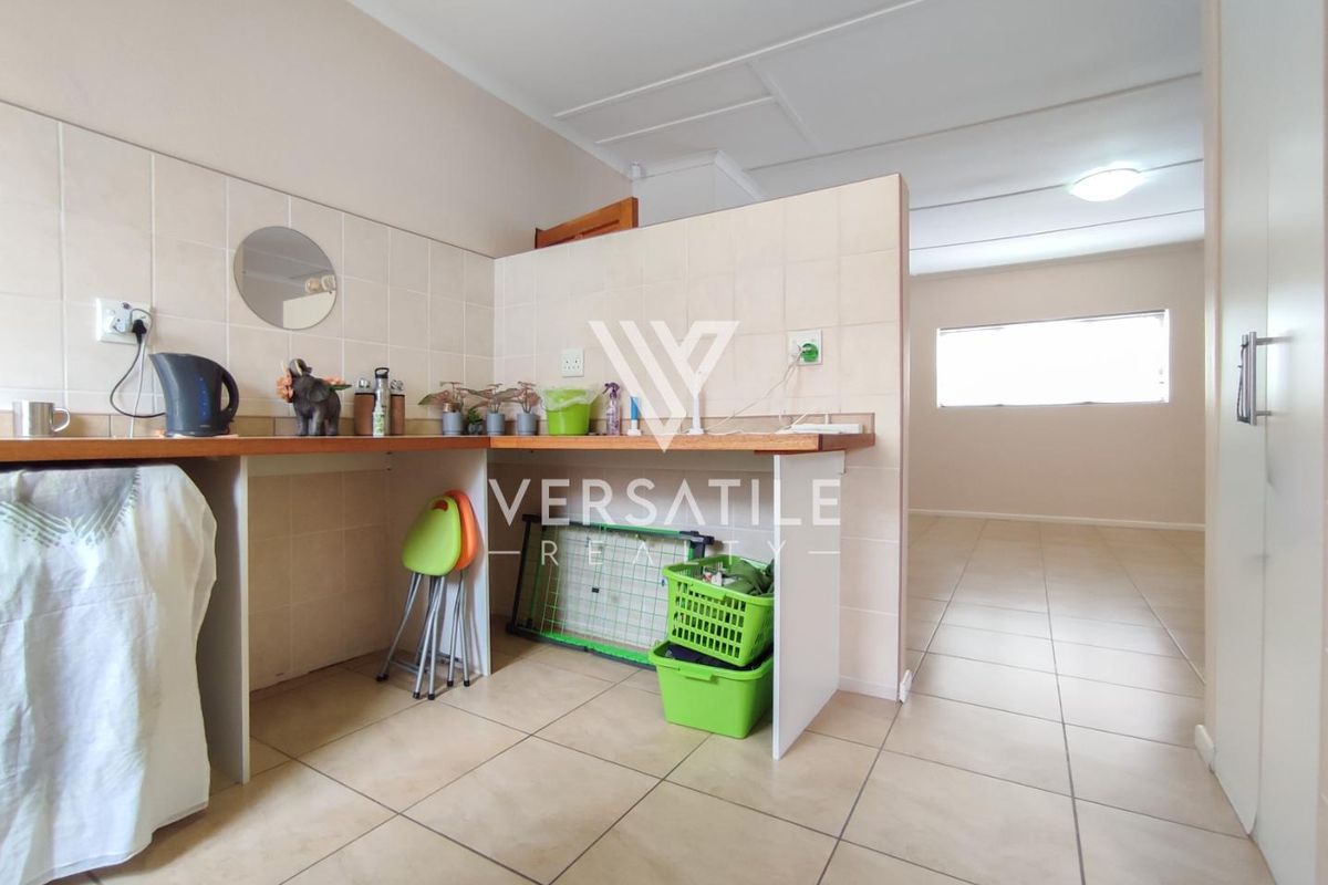 A functional kitchen area featuring tiled splashbacks, wooden countertops, and tiled flooring, seamlessly flowing into an adjacent living space.