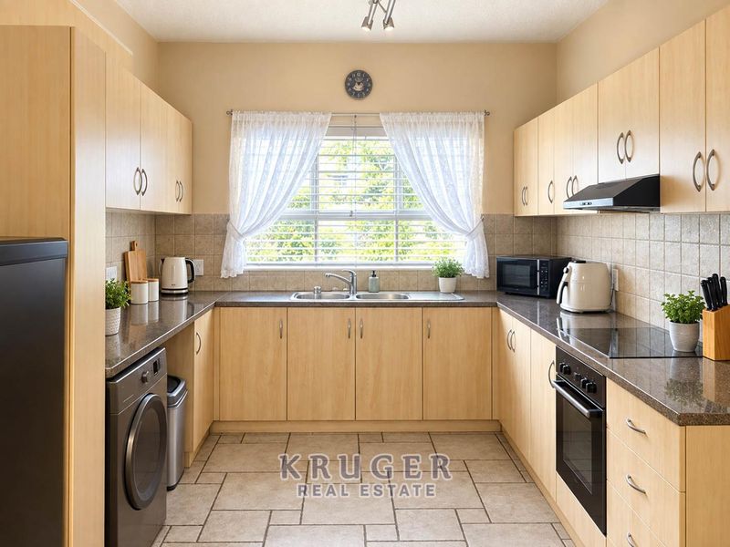 A functional U-shaped kitchen featuring light wood cabinetry, granite countertops, built-in oven, hob, extractor fan, and tiled flooring with ample natural light.