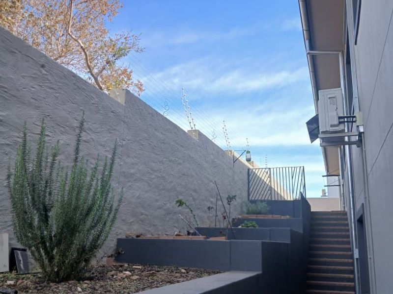 A side exterior view featuring a paved walkway, tiered retaining walls, a staircase, and an installed air conditioning unit against the building wall.
