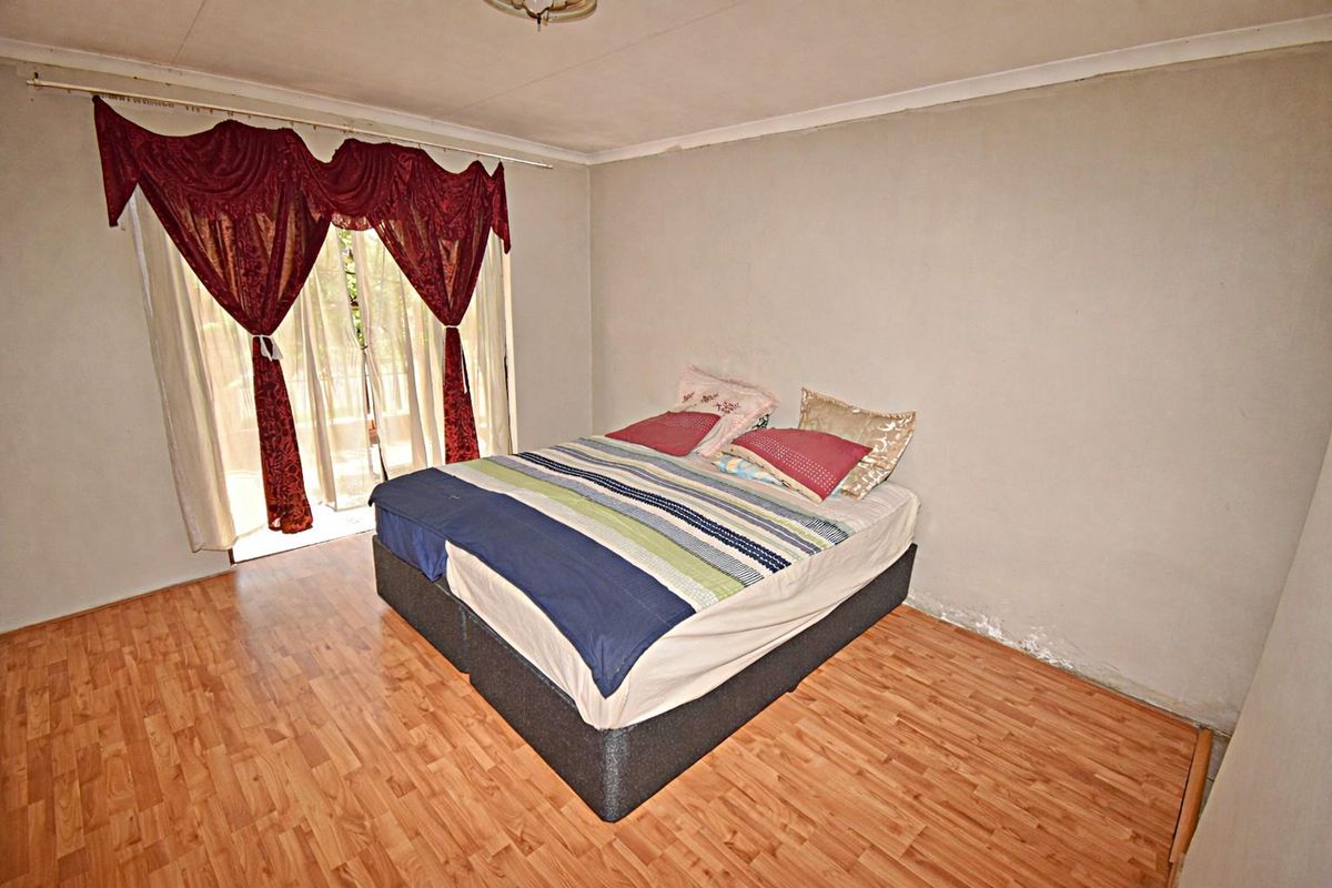 A bedroom featuring laminate flooring and sliding door access to the exterior, showing signs of wear and potential moisture issues on the wall.
