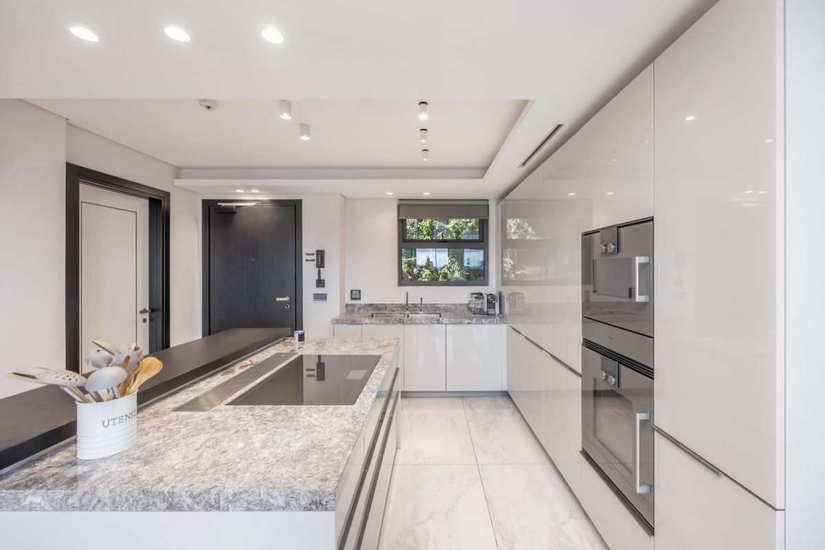 Modern kitchen featuring high-gloss cabinetry, stone countertops, a central island with an induction hob, and integrated built-in appliances.