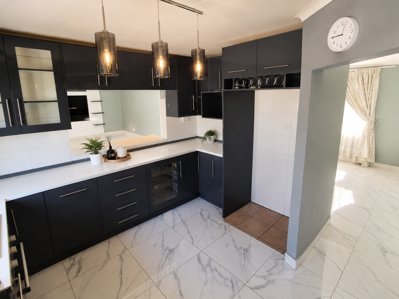 Modern kitchen featuring dark cabinetry, white quartz countertops, marble-look floor tiles, and integrated wine storage, offering a sleek and contemporary aesthetic.