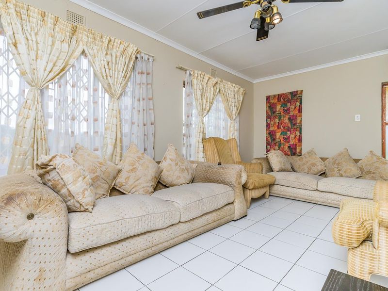 A living room featuring tiled flooring, a ceiling fan, and security gates on the windows, providing a functional and lived-in space.
