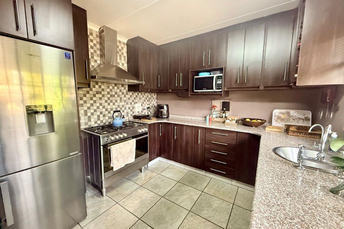 A functional kitchen featuring dark wood cabinetry, granite-look countertops, a stainless steel gas stove with extractor fan, and tiled flooring.