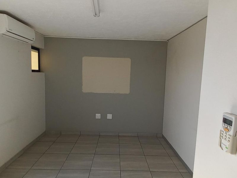 A functional office space featuring tiled flooring, a wall-mounted air conditioning unit, and neutral wall finishes.