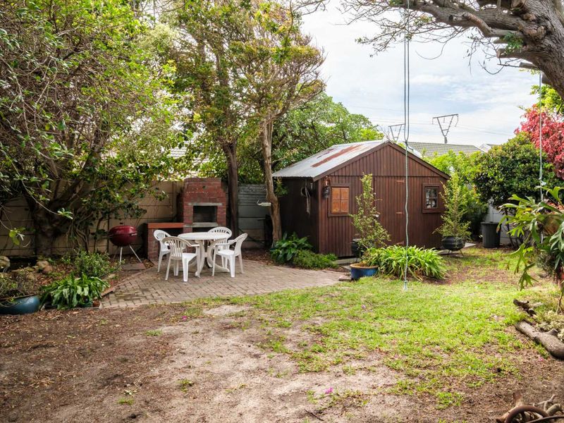 A private garden area featuring a paved patio, a built-in brick braai, and a wooden storage shed surrounded by mature trees.