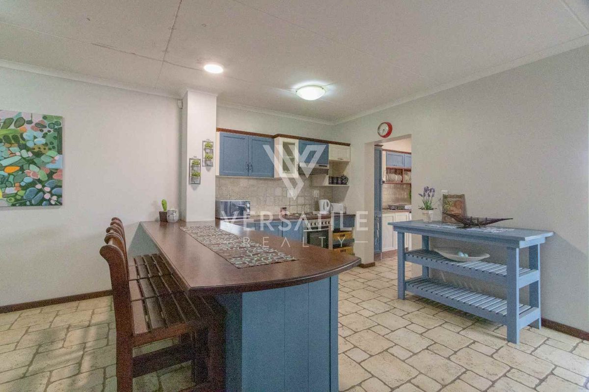 A functional kitchen area featuring blue cabinetry, a built-in breakfast bar, and tiled flooring, with an adjacent scullery visible through the doorway.