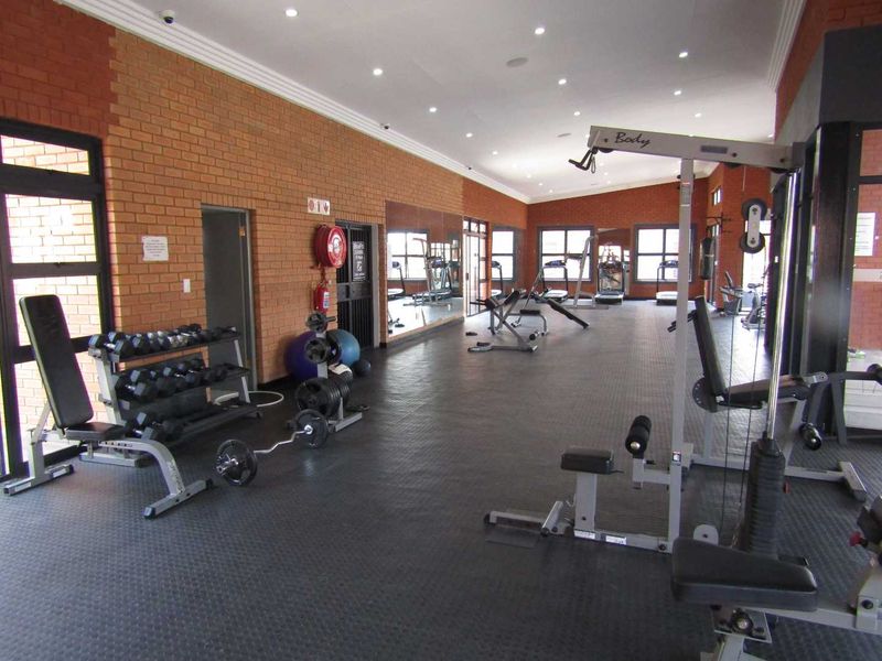 A well-maintained communal gym facility featuring exposed brick walls, rubberized flooring, recessed lighting, and wall-mounted mirrors.