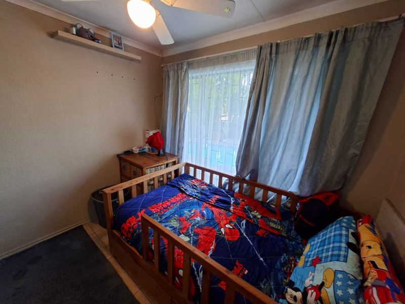 A bedroom featuring a ceiling fan, a built-in wall shelf, and a window fitted with security bars.