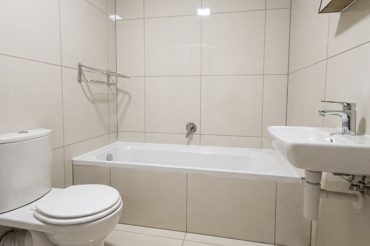 A clean, modern bathroom featuring neutral wall and floor tiles, a built-in bathtub, a wall-mounted basin with chrome fixtures, and a standard toilet.