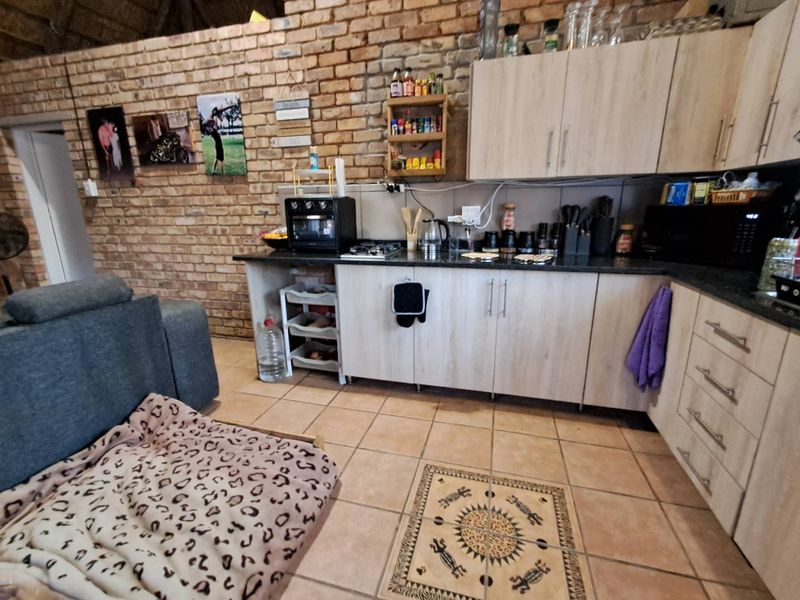 Open plan kitchen area featuring exposed brick walls, laminate cabinetry, granite countertops, and ceramic tiled flooring in a cottage-style setting.