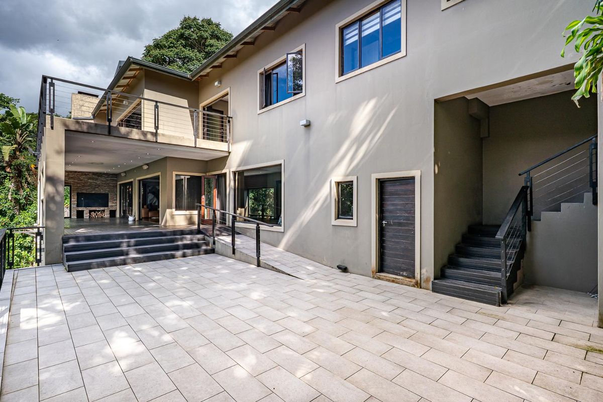 Spacious rear exterior view featuring a paved patio, covered entertainment area, external staircase, and ramp access to the multi-level guest house structure.