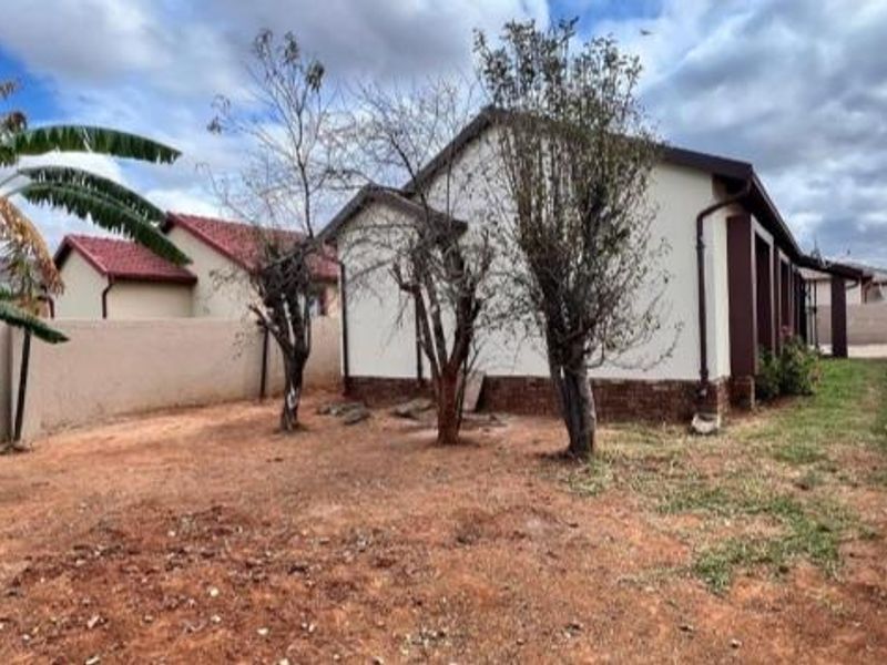 Rear exterior view of the property featuring a large garden area with perimeter walling and established trees.