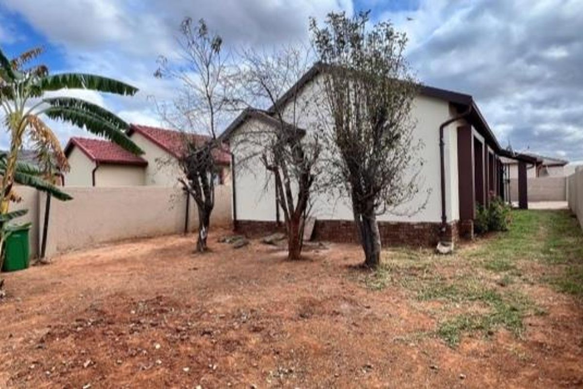 Rear exterior view of the property featuring a large garden area with perimeter walling and established trees.