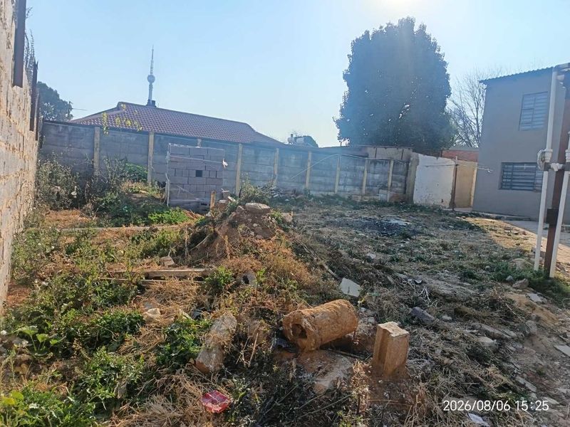 A view of the rear yard area featuring a perimeter boundary wall and unmaintained ground surface with visible debris.