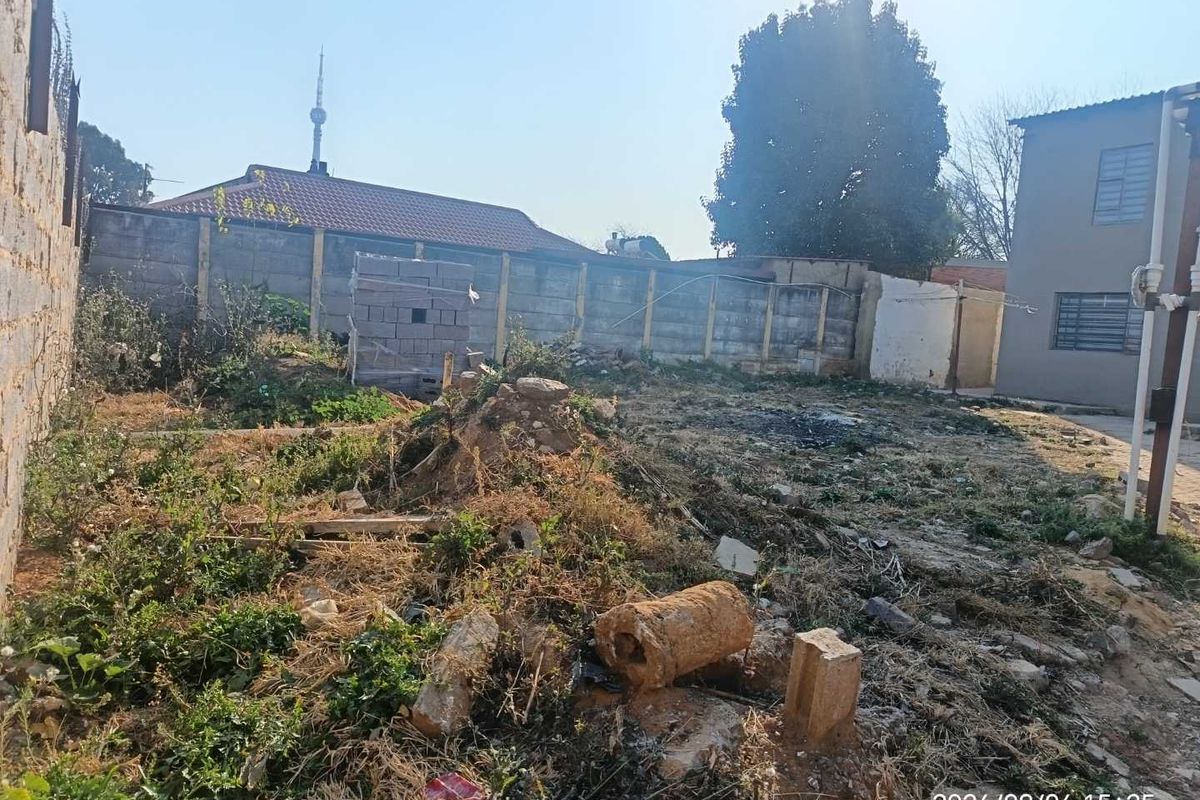 A view of the rear yard area featuring a perimeter boundary wall and unmaintained ground surface with visible debris.