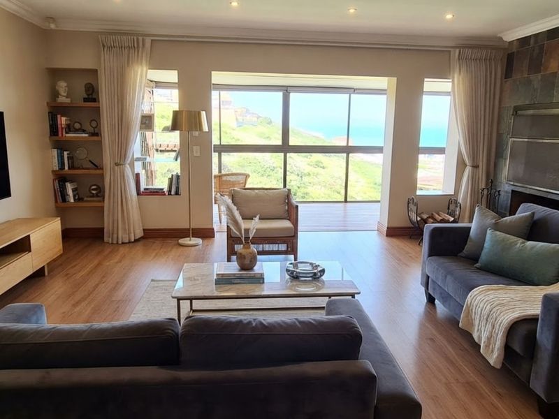 Spacious living room featuring laminate flooring, a stone-clad fireplace, built-in shelving, and large sliding doors opening to a scenic coastal view.