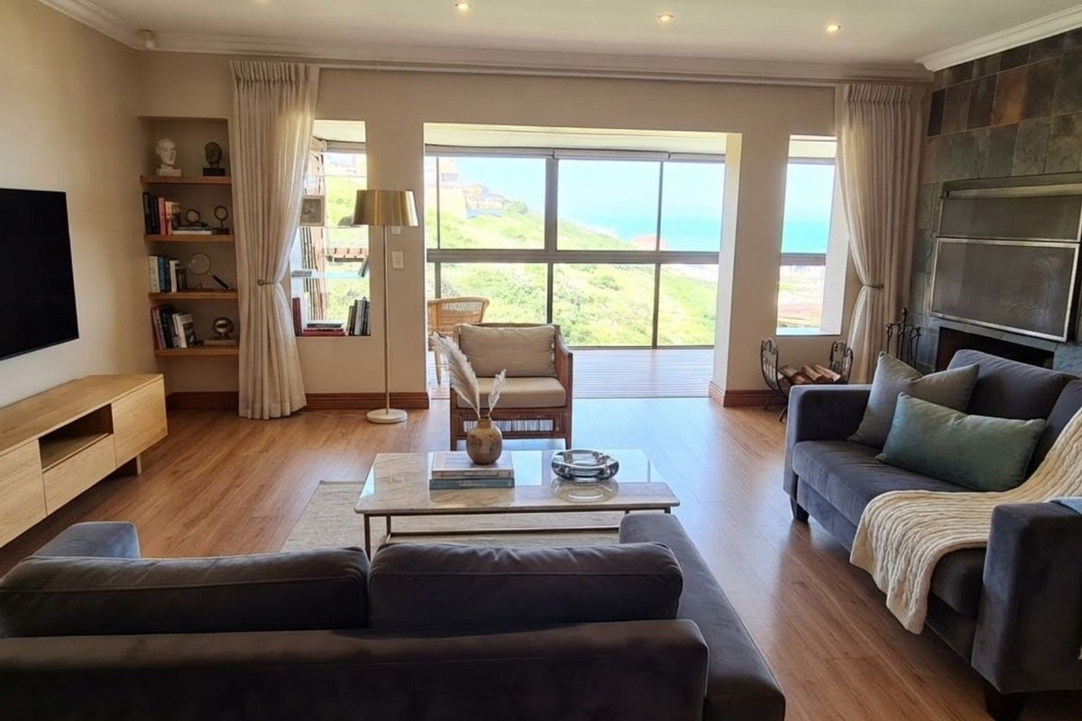Spacious living room featuring laminate flooring, a stone-clad fireplace, built-in shelving, and large sliding doors opening to a scenic coastal view.