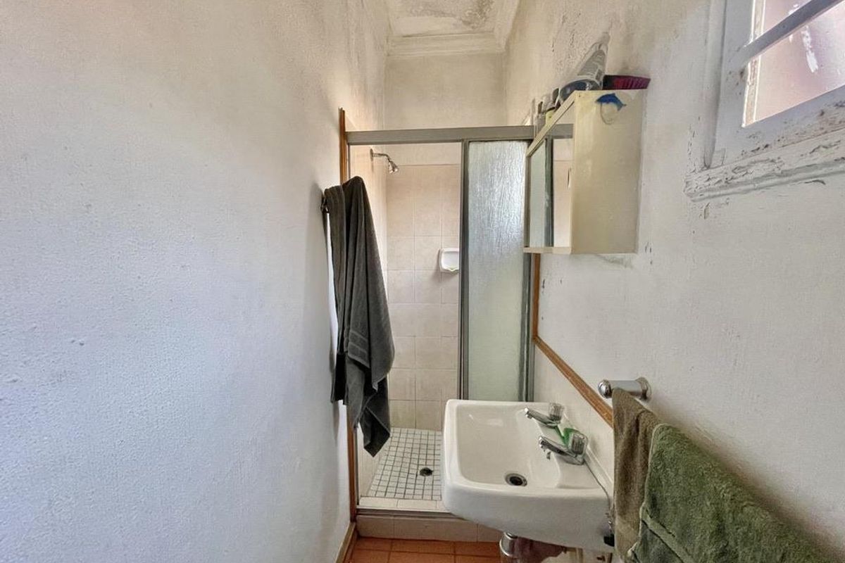A compact bathroom featuring a shower cubicle, wall-mounted basin, and tiled flooring, requiring cosmetic updates and maintenance to the ceiling and window frame.