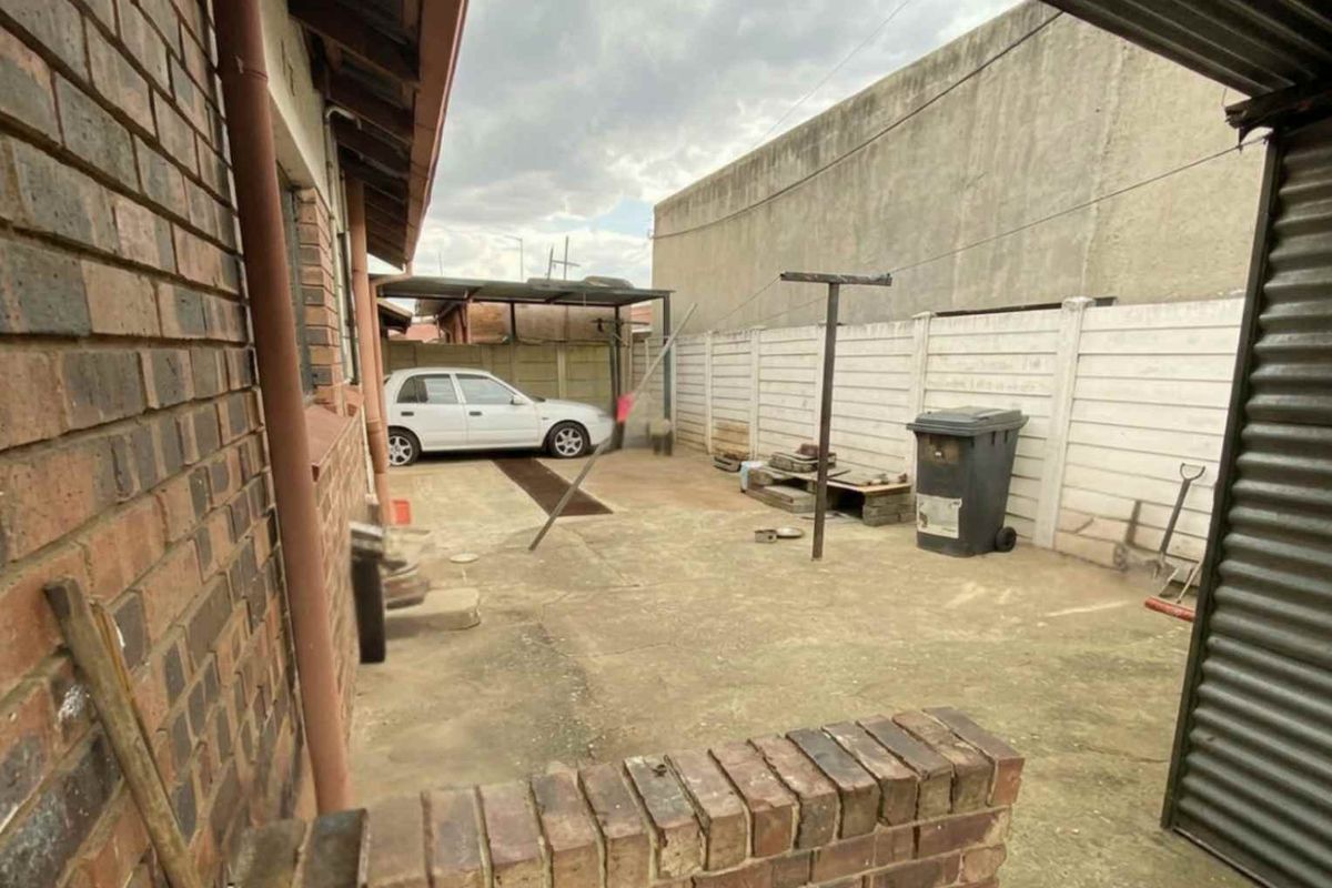 A paved rear courtyard area featuring a brick boundary wall, concrete perimeter fencing, and a metal clothesline structure.