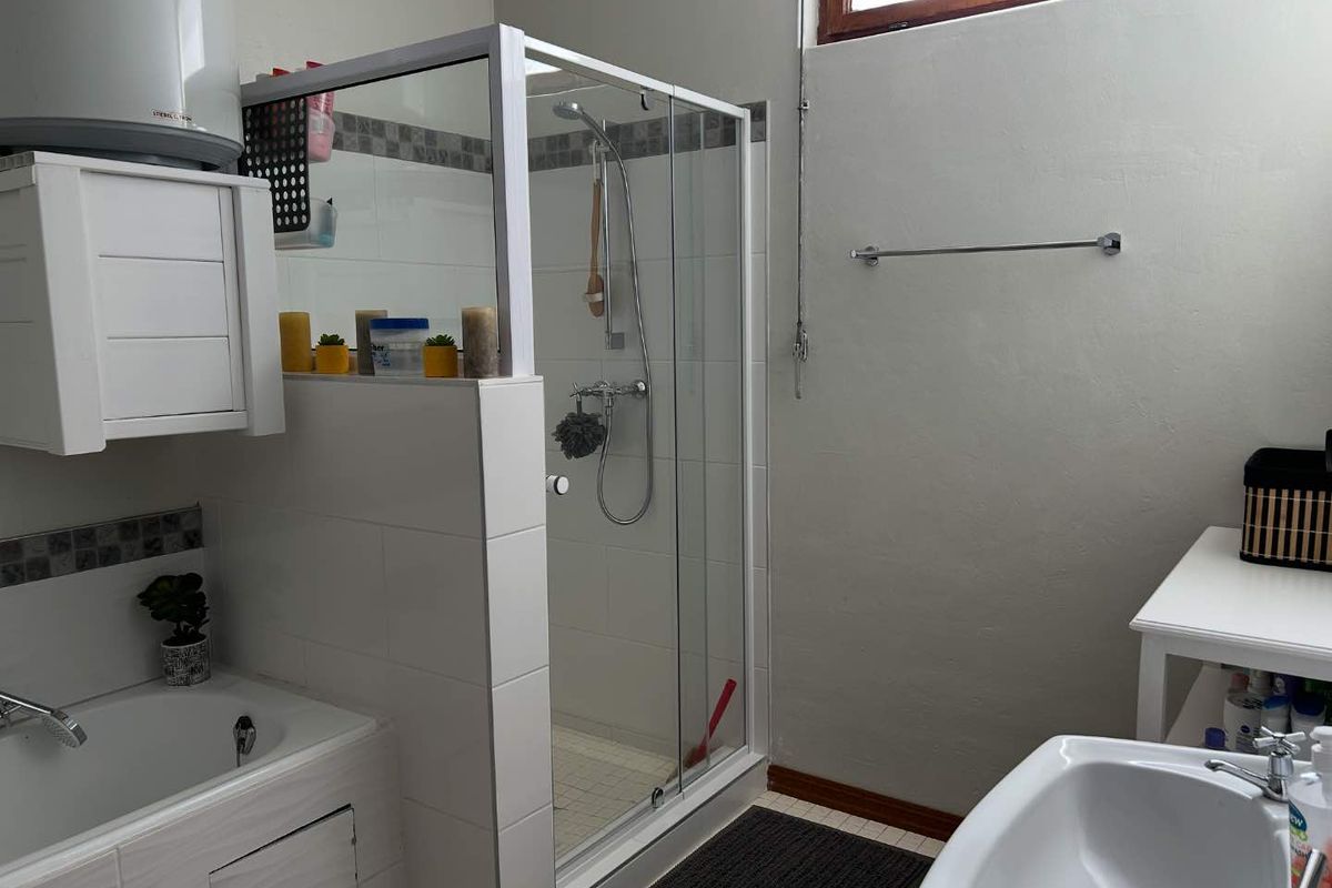 A functional bathroom featuring a glass-enclosed shower, built-in bathtub, and vanity basin with tiled splashbacks and neutral finishes.