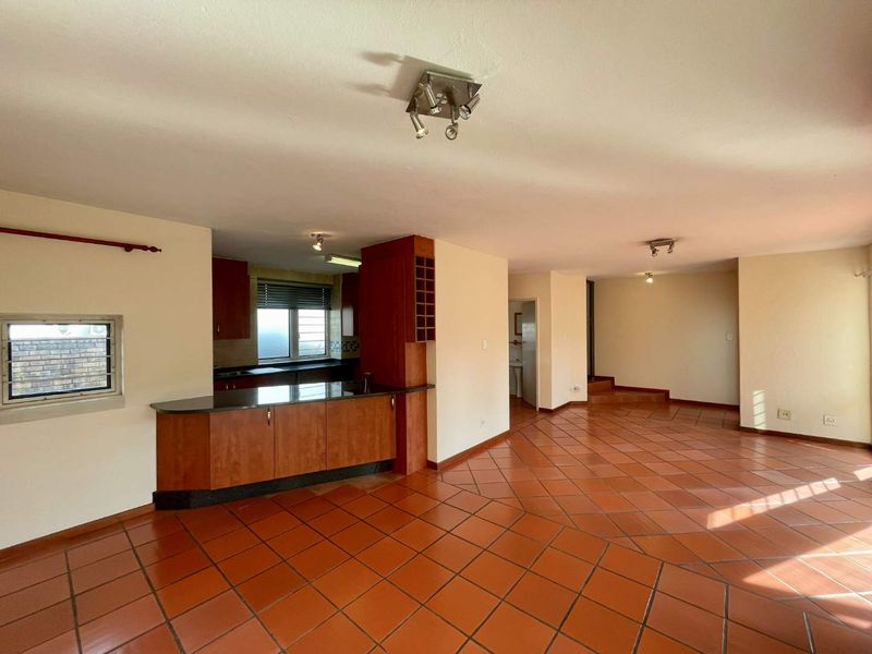 Spacious open-plan living and kitchen area featuring terracotta floor tiles, built-in cabinetry with granite countertops, and a breakfast bar.