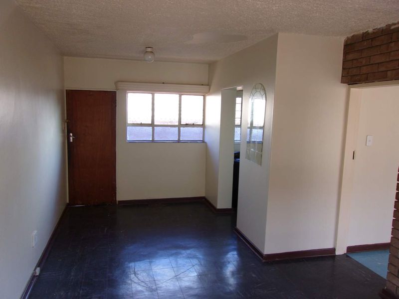 An empty living area featuring dark tiled flooring, a timber door, and exposed brick accents, offering a blank canvas for renovation.
