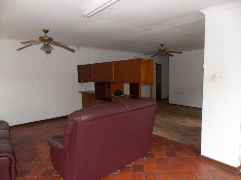 Spacious living area featuring terracotta floor tiles, built-in brick bar, and dual ceiling fans, offering a dated layout ready for modernization.