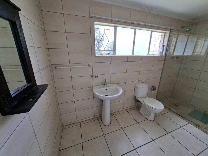 A functional bathroom featuring a pedestal basin, toilet, and a walk-in shower enclosure with neutral ceramic tiling throughout.