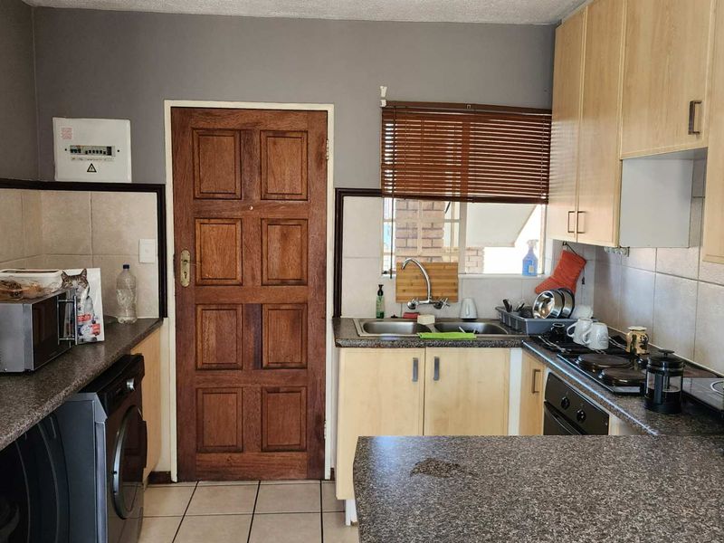 Functional kitchen featuring laminate cabinetry, granite countertops, double basin sink, built-in oven, and electric hob with tiled backsplash and flooring.