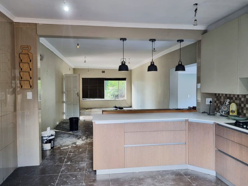Open plan kitchen and living area featuring modern cabinetry and pendant lighting, currently undergoing renovation with unfinished flooring and exposed electrical fixtures.