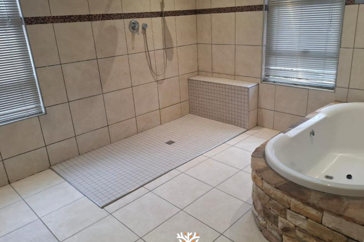 A spacious bathroom featuring a walk-in shower with mosaic tile accents and a stone-clad built-in bathtub.