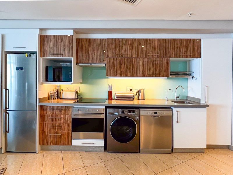 Modern kitchen featuring wood-grain cabinetry, integrated appliances, a sleek electric hob, and a glass splashback, offering a clean and functional cooking space.