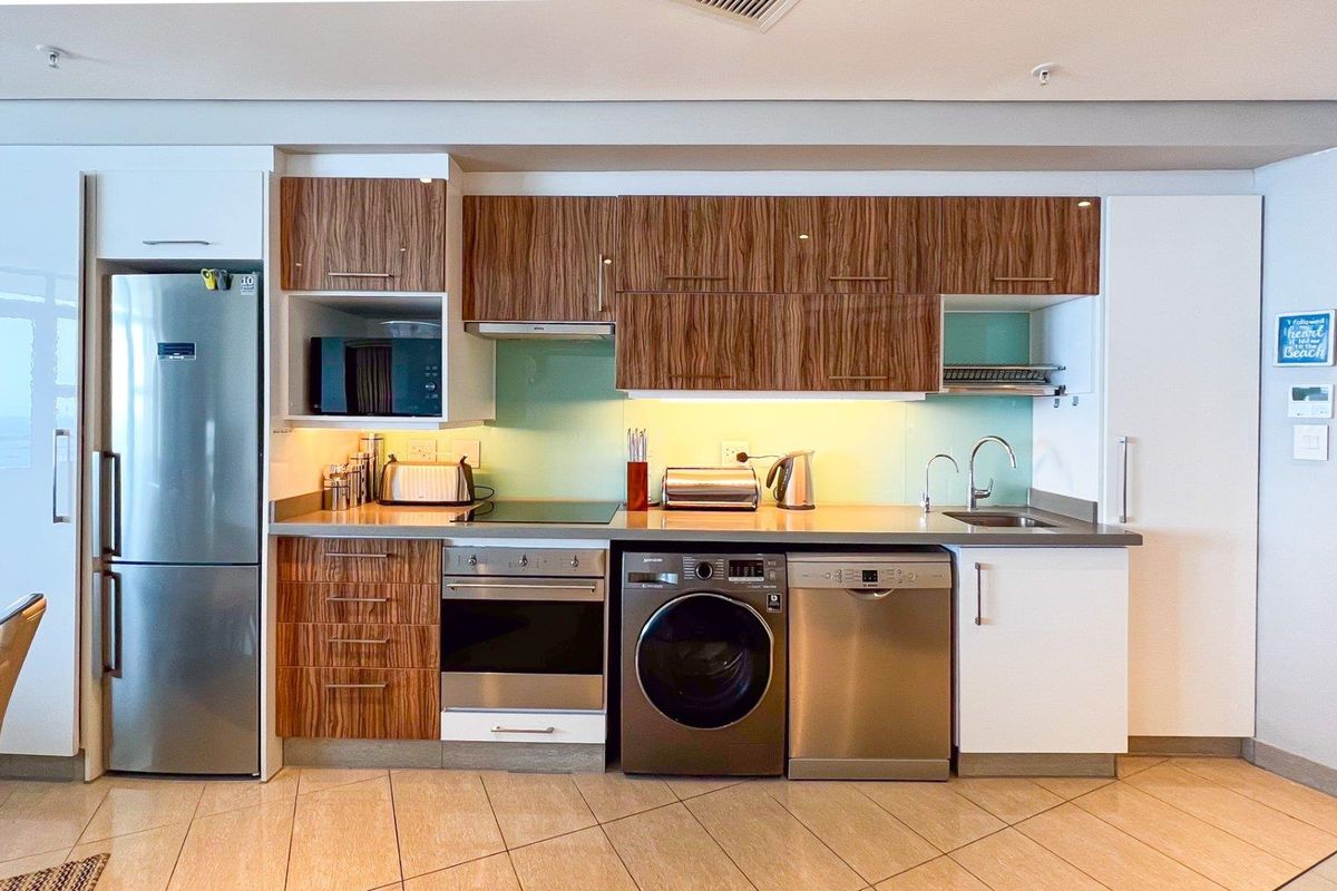 Modern kitchen featuring wood-grain cabinetry, integrated appliances, a sleek electric hob, and a glass splashback, offering a clean and functional cooking space.