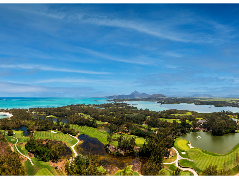 An expansive aerial view showcasing a lush golf course, surrounding water bodies, and a scenic coastal landscape under a clear blue sky.
