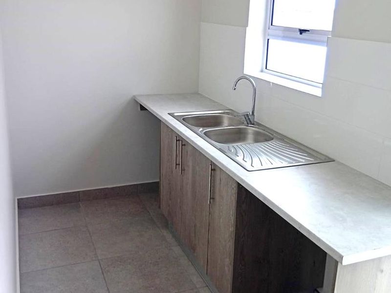 A clean and functional laundry area featuring a stainless steel double sink, built-in base cabinetry, and tiled flooring.