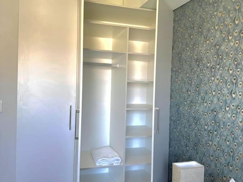A bedroom featuring a modern white built-in wardrobe with shelving and hanging space, complemented by a decorative peacock-patterned feature wall.