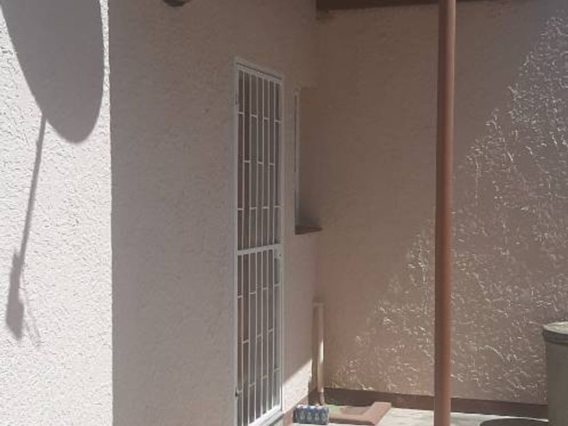 A covered outdoor patio area featuring a corrugated metal roof, security gate, and concrete flooring, suitable for a small seating area.