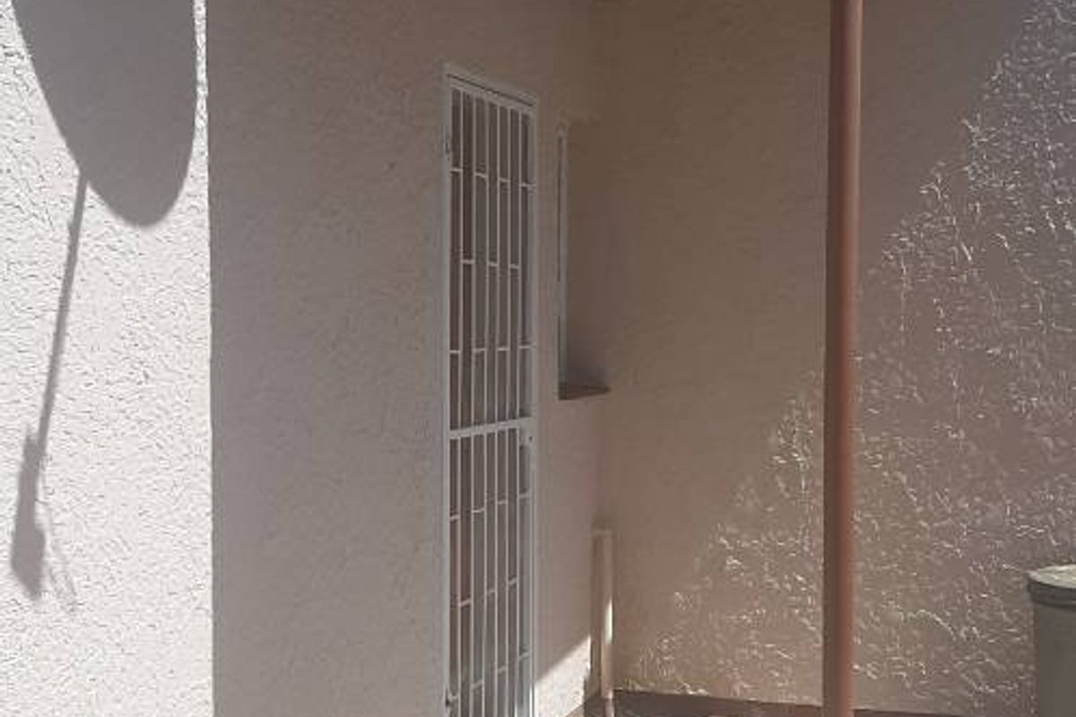 A covered outdoor patio area featuring a corrugated metal roof, security gate, and concrete flooring, suitable for a small seating area.