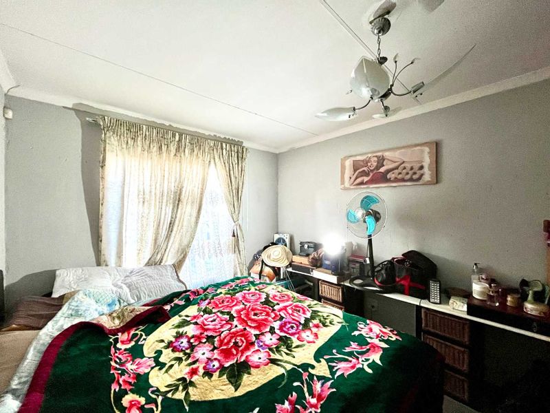 A bedroom featuring a ceiling fan and curtain rails, showing signs of wear including ceiling cracks and peeling paint.