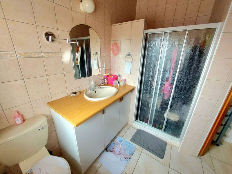 A functional bathroom featuring a vanity cabinet with a basin, a shower enclosure, and a toilet, finished with neutral wall and floor tiles.