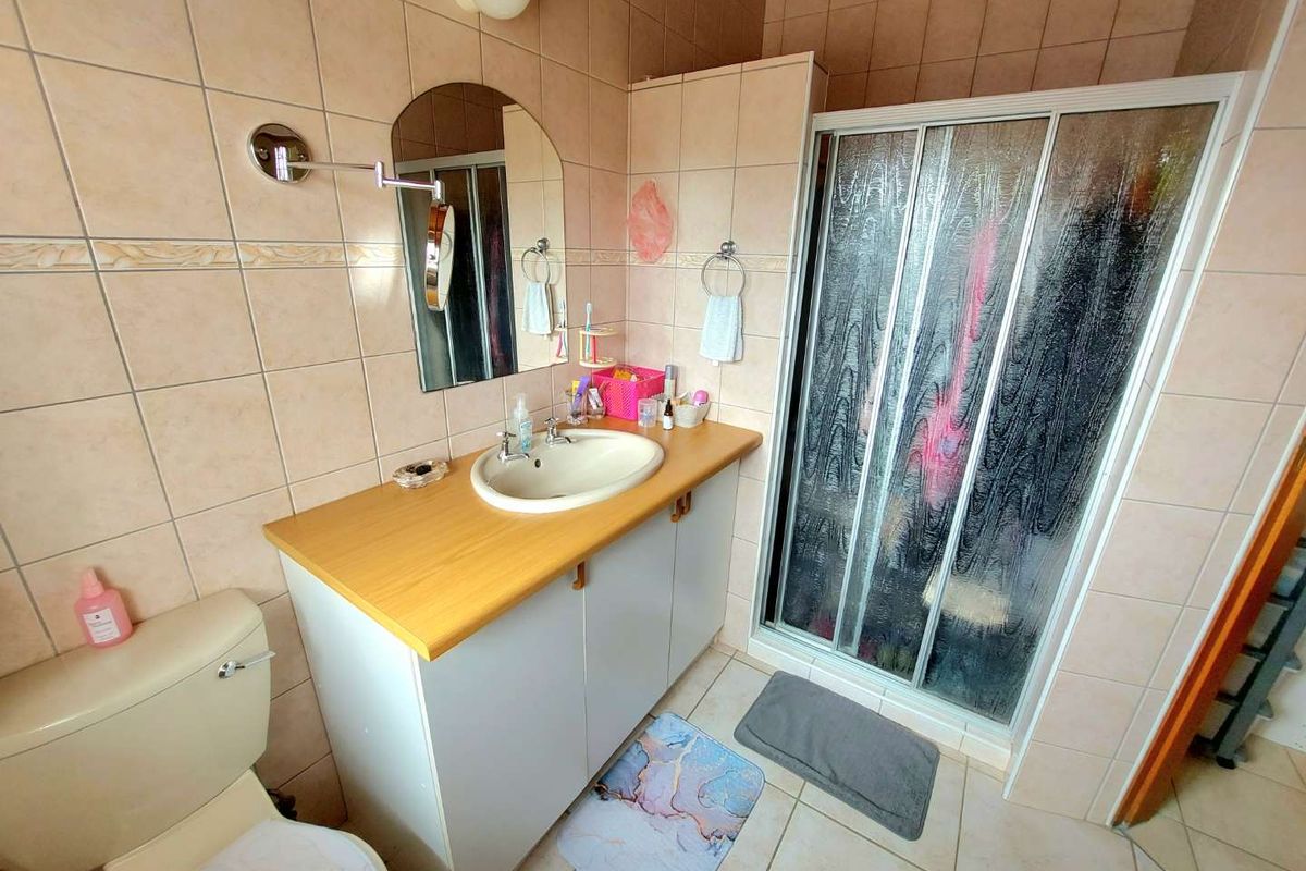 A functional bathroom featuring a vanity cabinet with a basin, a shower enclosure, and a toilet, finished with neutral wall and floor tiles.